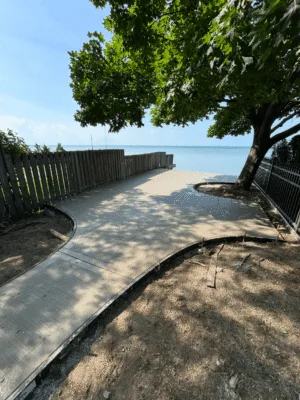 Freshly poured concrete walkway leading to the waterfront under a shaded tree in Windsor.